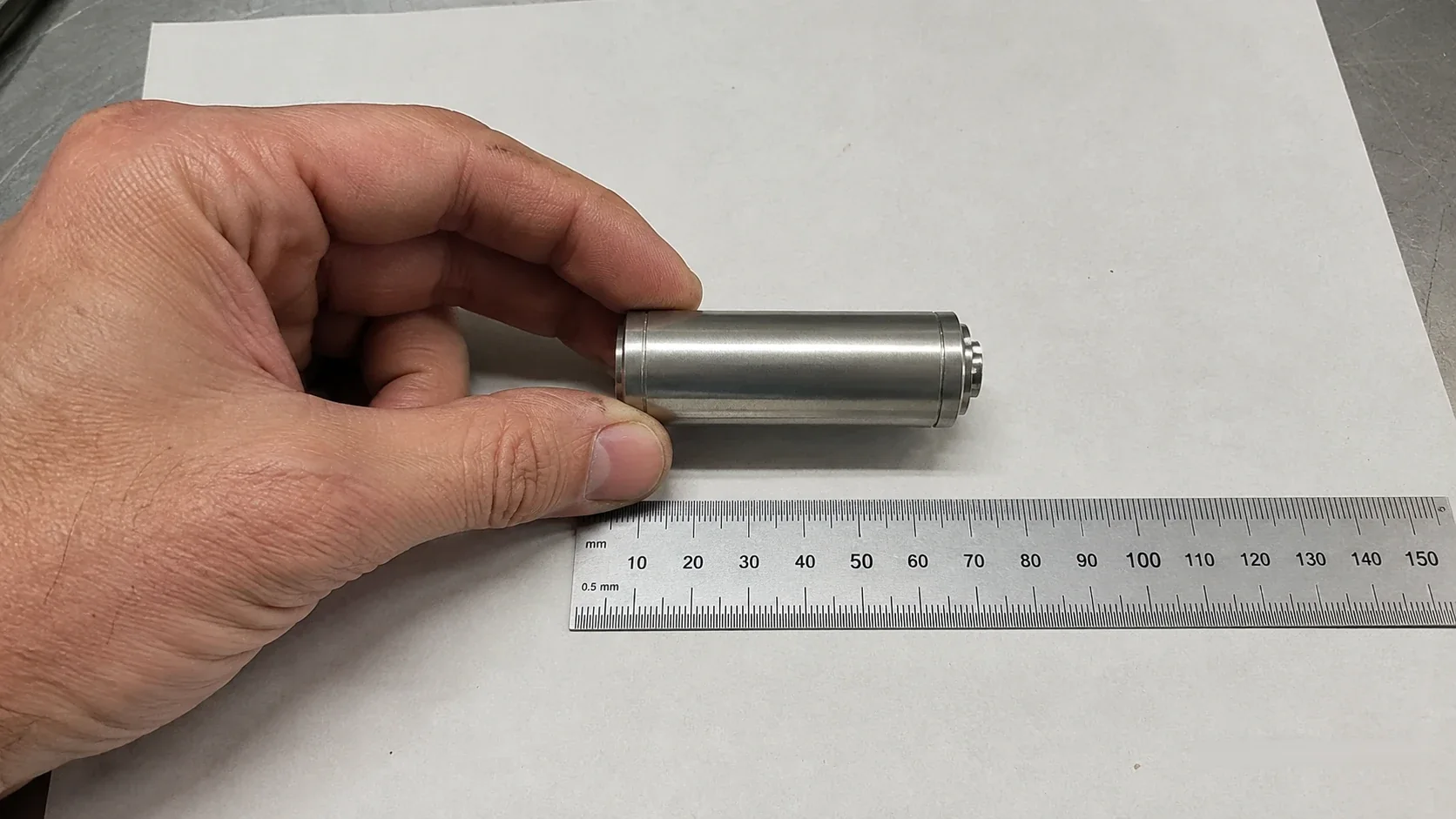 Manufactured cylindrical pump housing held in a hand next to a ruler for scale